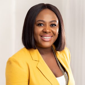 Mojolaoluwa Aderemi-Makinde smiles at the camera. She is wearing a yellow blazer and is a Black woman with a short bob, set against a professional neutral background.