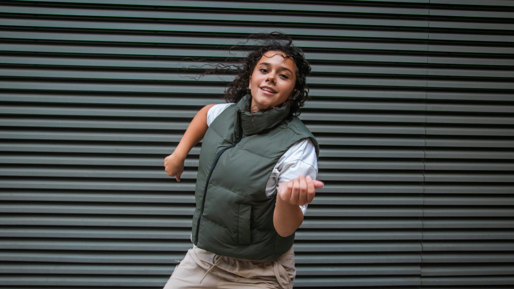 Dance Summer School promotional image for Summer @ Impact, featuring a happy young dancer in an outdoor setting freestyling in hip-hop dance and smiling to camera invitingly.